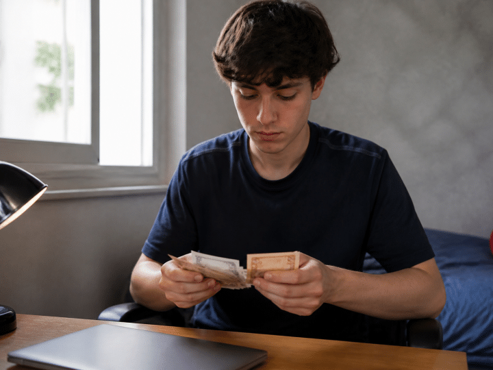 Adolescent assis a un bureau tenant des billets de banque