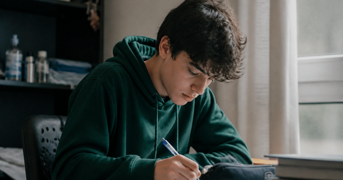 Adolescent assis a un bureau, stylo en main, etudiant