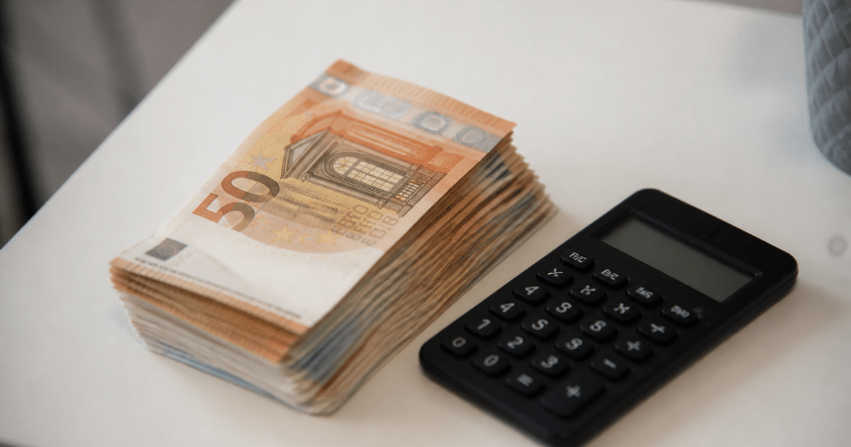 Liasse de billets euros posee sur table blanche avec calculatrice