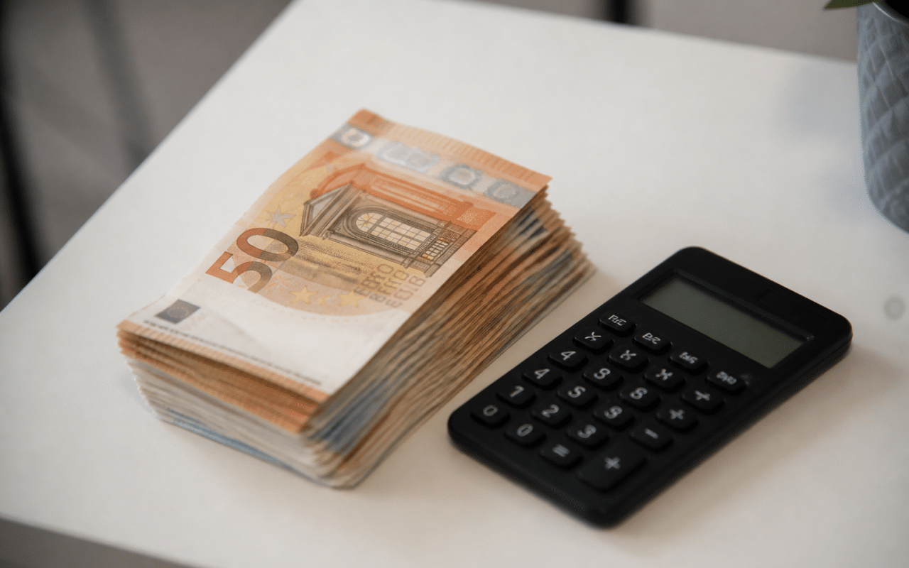 Liasse de billets euros posee sur table blanche avec calculatrice