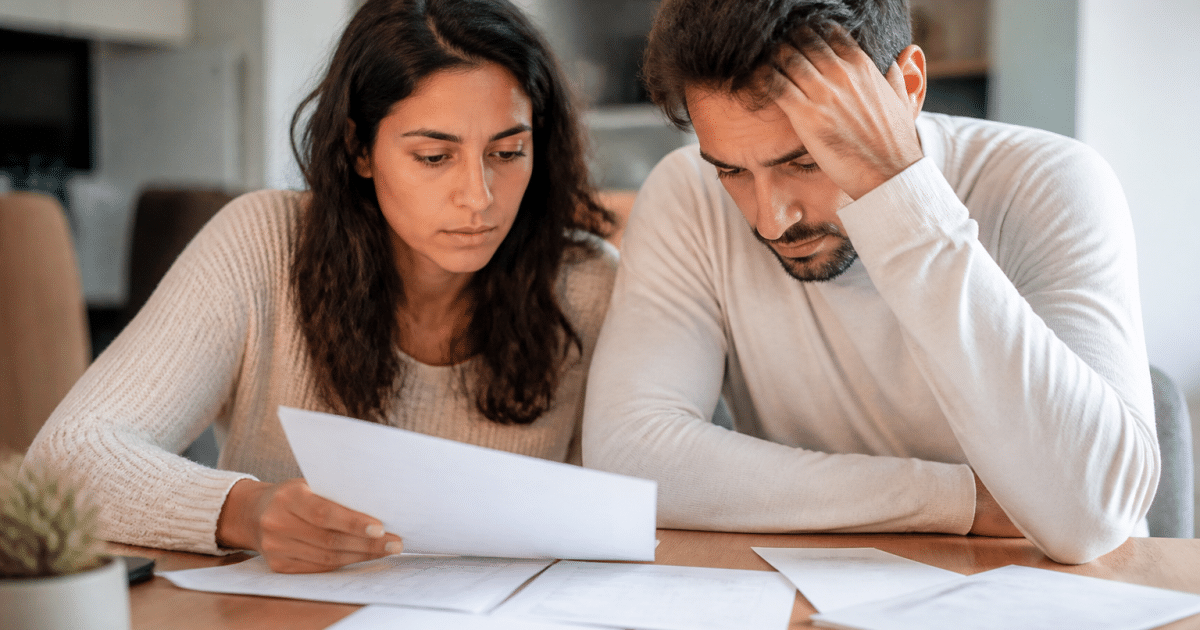 Couple consultant des documents financiers à table, factures étalées.