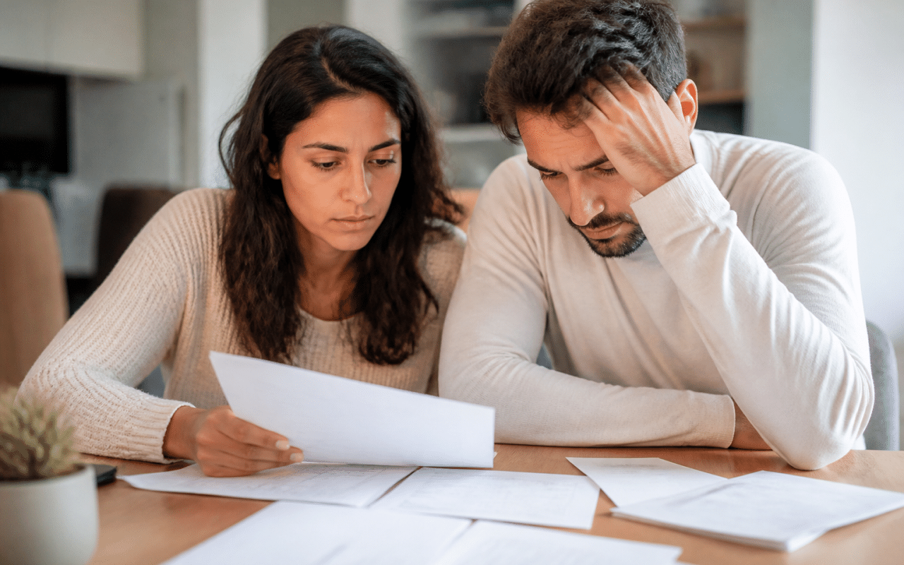 Couple consultant des documents financiers à table, factures étalées.