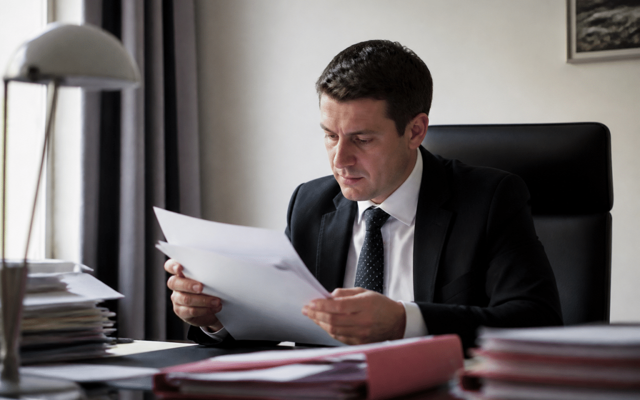 Huissier en costume examinant des documents financiers à son bureau.