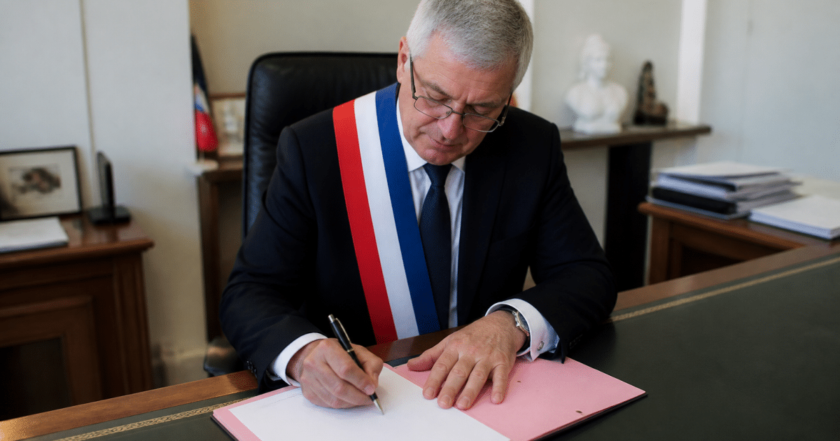 Maire assis a son bureau signant un document officiel