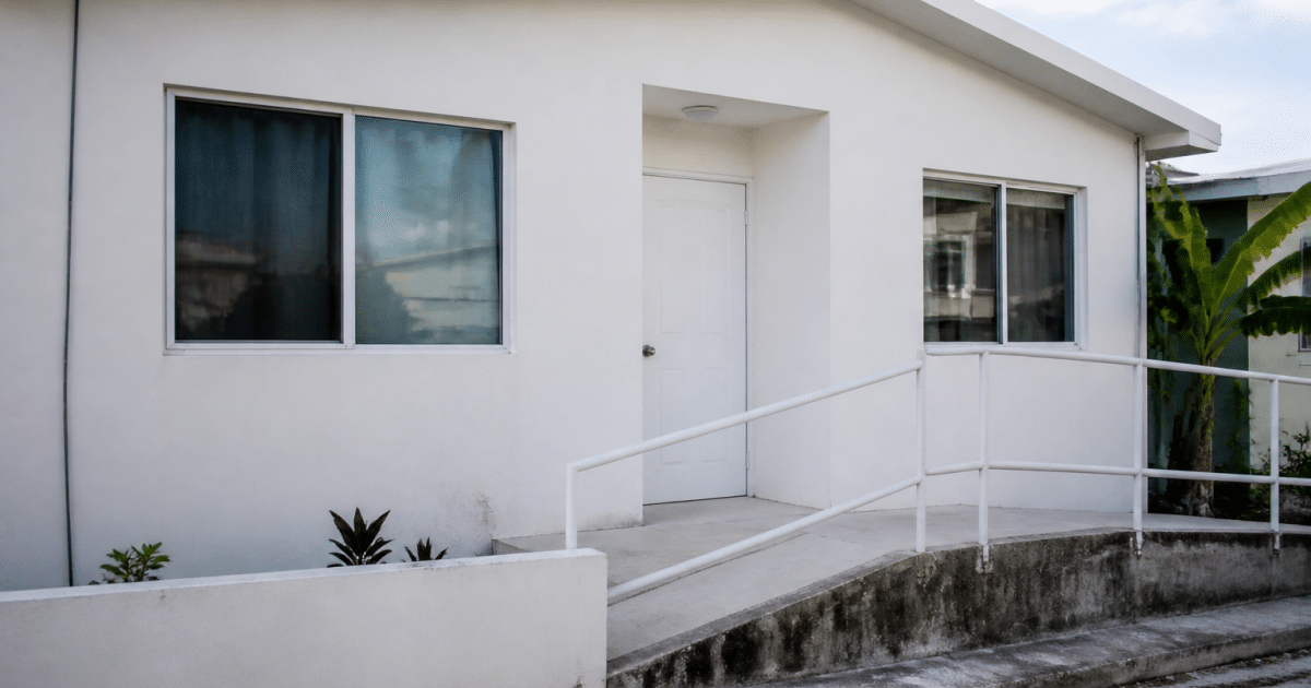 Facade d'une petite maison blanche sans etages avec rampe d'acces.