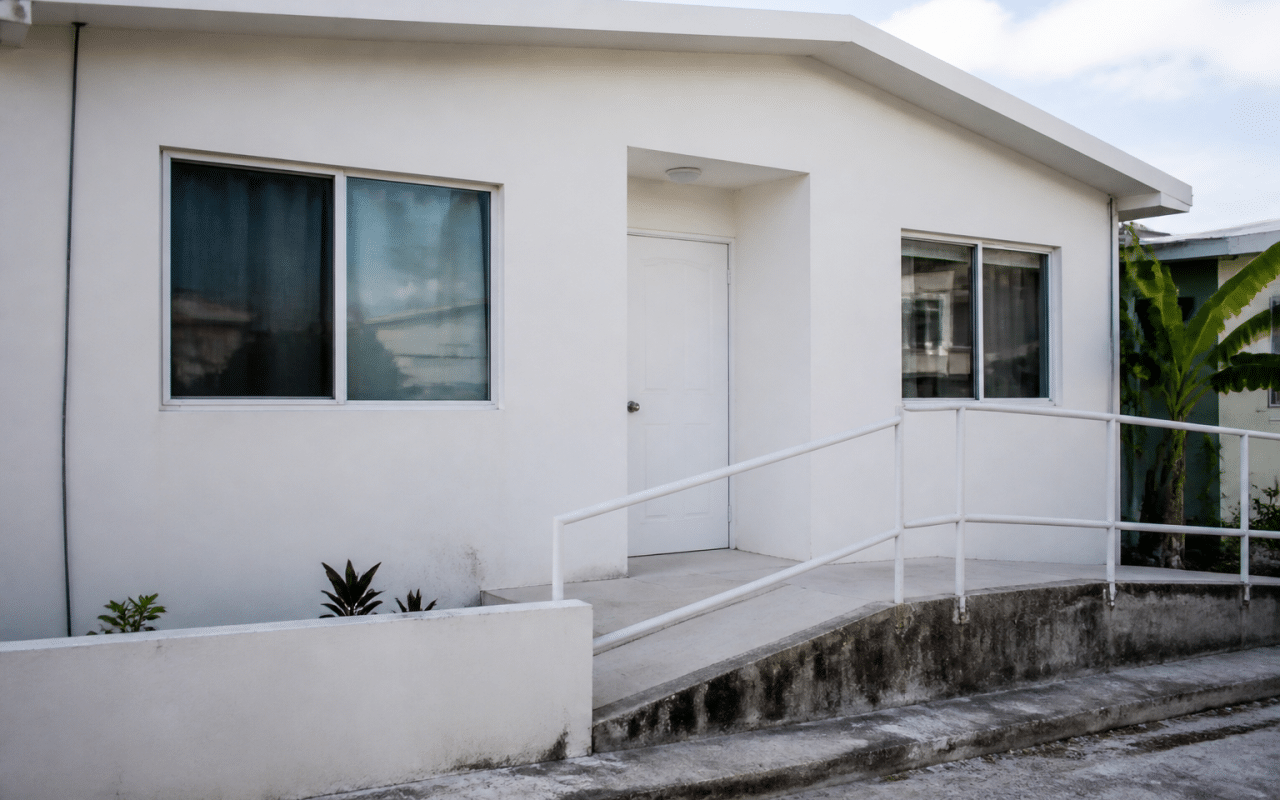 Facade d'une petite maison blanche sans etages avec rampe d'acces.