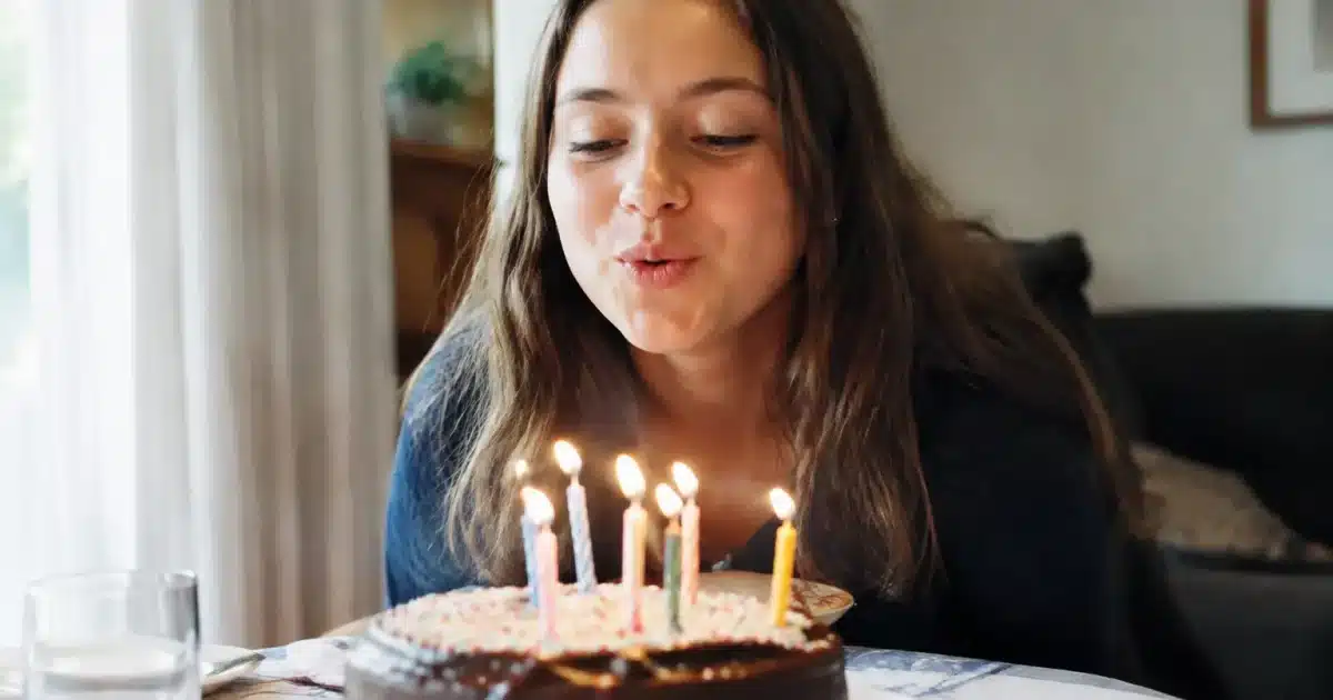 Jeune fille souriante soufflant des bougies devant un gateau